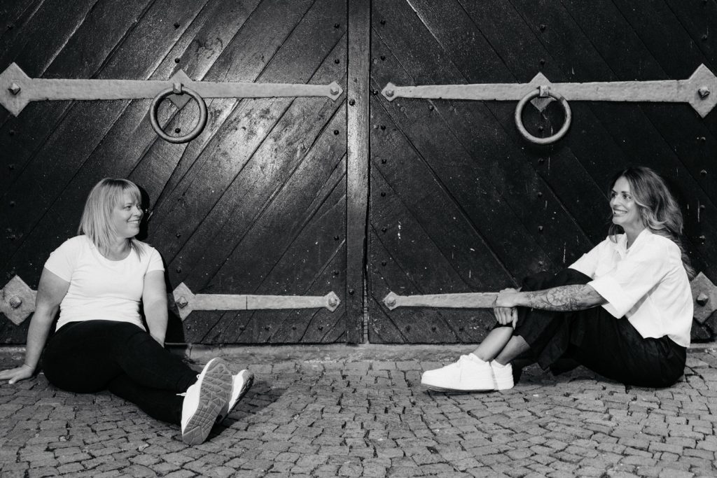 Paar sitzt vor Holztor beim Fotoshooting in Aschaffenburg und lacht sich an