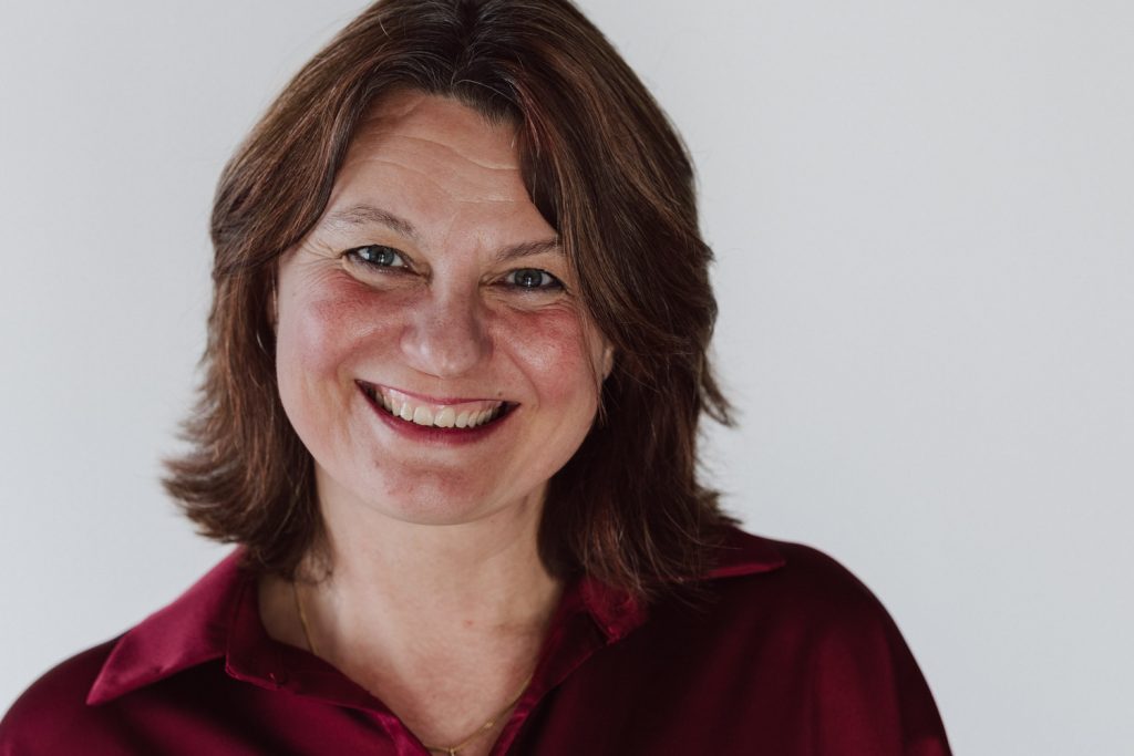 Business Portrait Aschaffenburg, lächelnde Frau in roter Bluse vor hellem Studiohintergrund